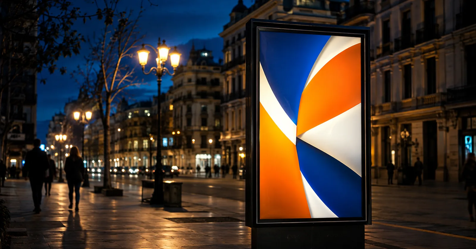 Mupi publicitario iluminado de noche en una avenida española con peatones