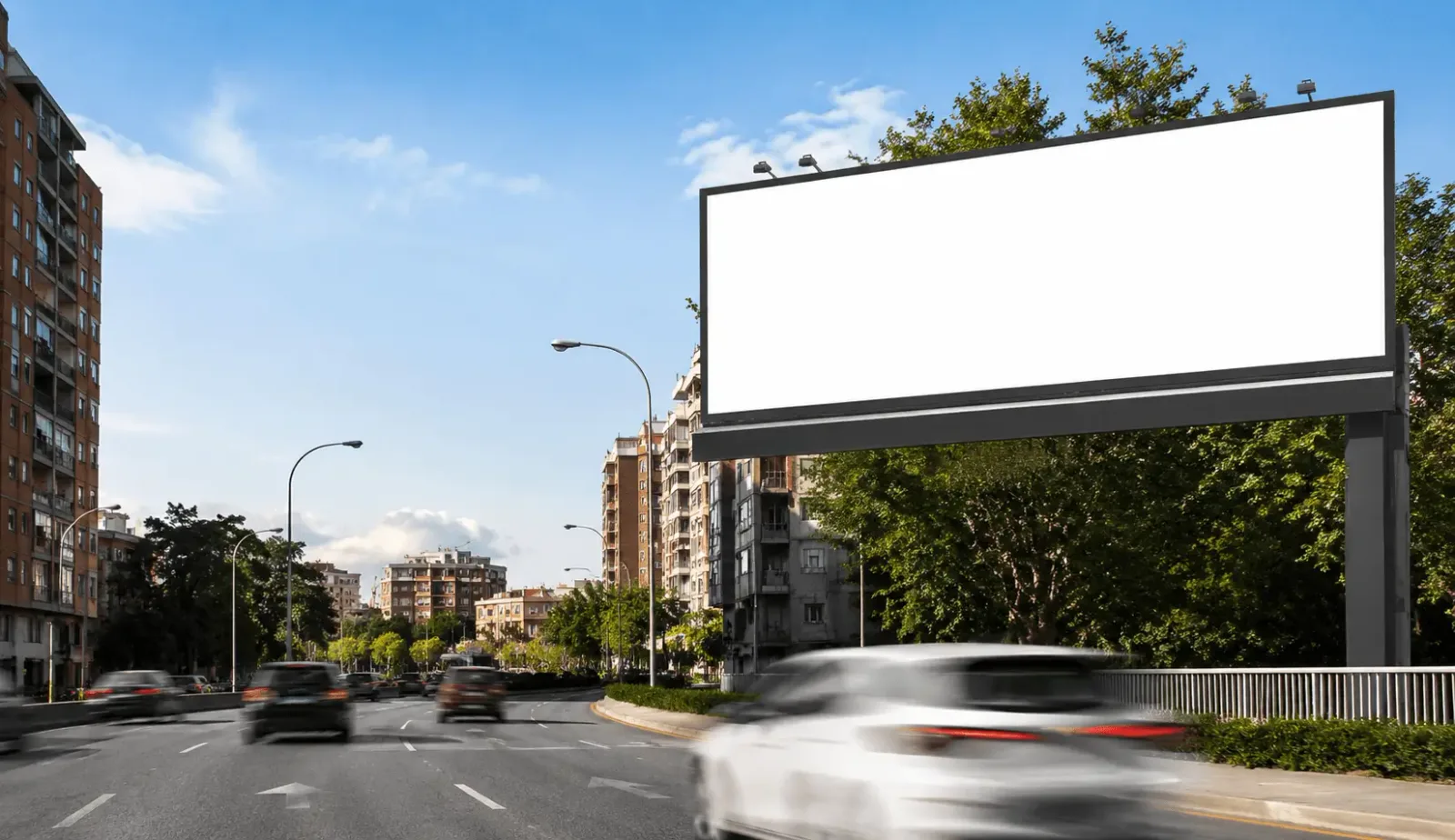 Valla publicitaria de gran formato en una avenida de acceso a un barrio comercial español con tráfico al fondo