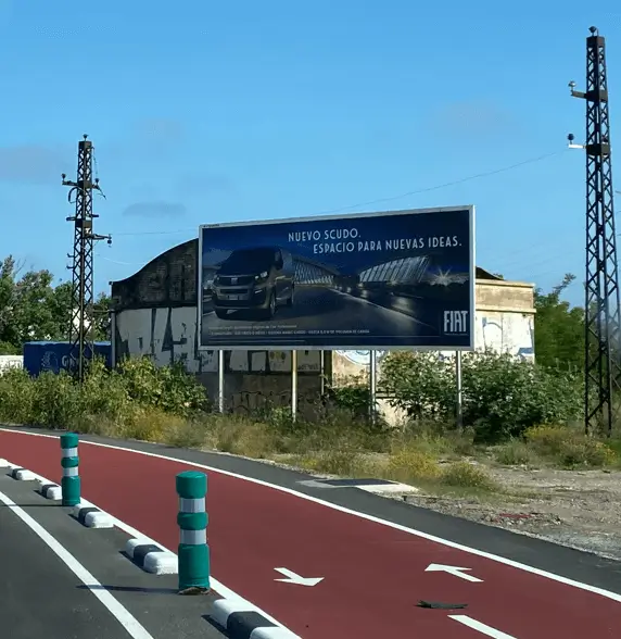 Valla de 8 x 3 metros junto al carril bici de la avenida del Ingeniero Andoni Sarasola, con torres de alta tensión al fondo, en el barrio Biensa de Puerto de Sagunto